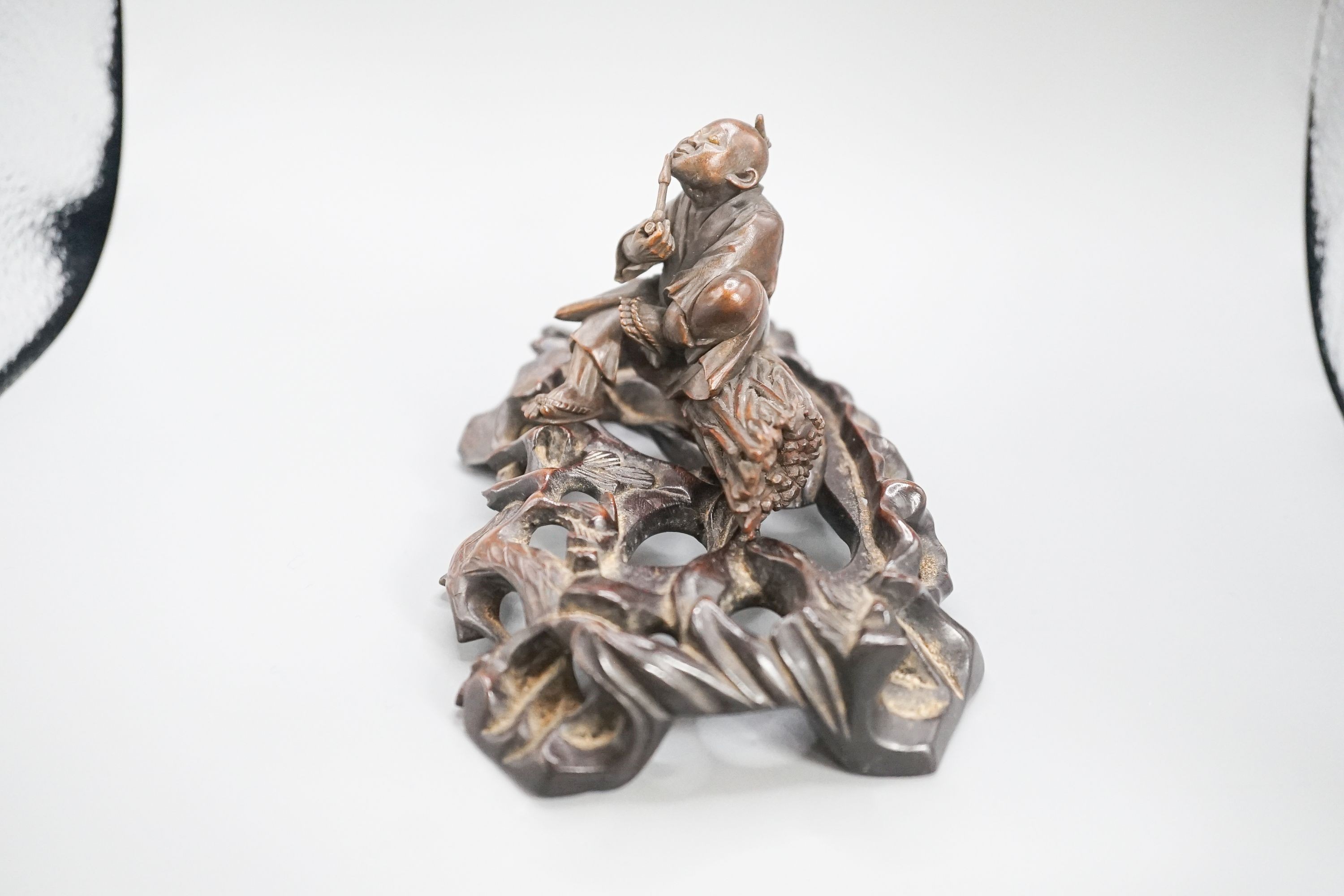 A 19th century Japanese wood okimono of a seated man smoking a pipe, signed, 7.8cm on a later hardwood stand